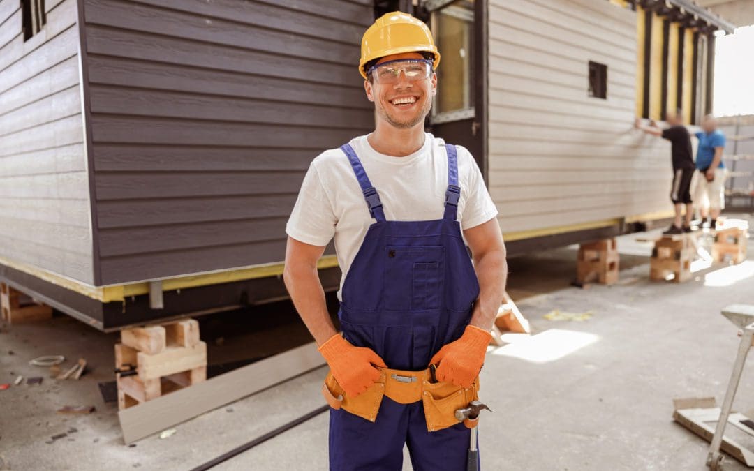 Handsome young man construction worker wearing safety helmet and work overalls while looking at camera and smiling