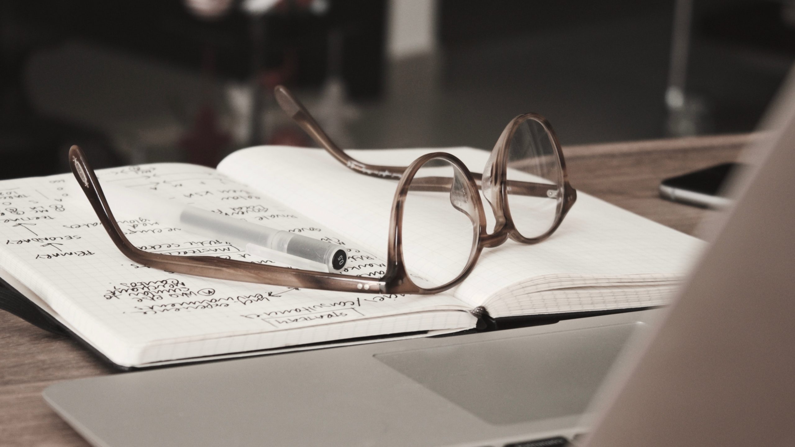 glasses lying on top of an open notebook on desk in front of laptop